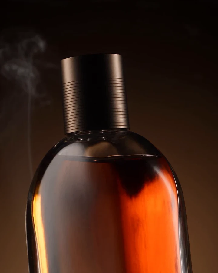 The Ambre Fumé flacon with a ribbed metal cap, amber juice glowing in warm light