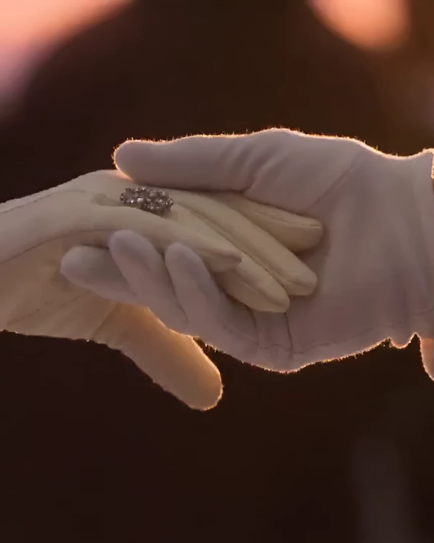A gloved hand with a diamond ring resting in a gentleman's white glove