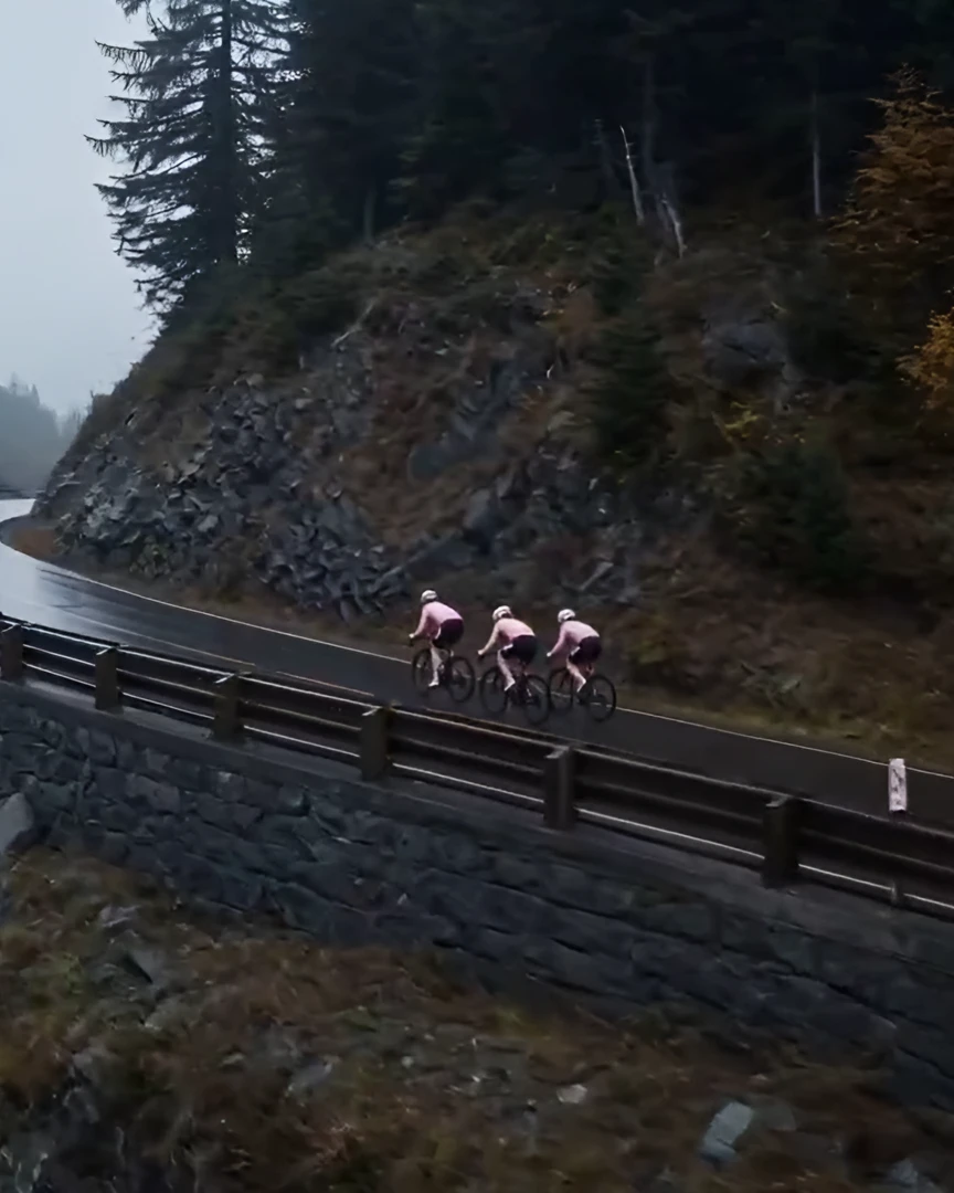Riders on a road cut into a forested mountainside, seen from above