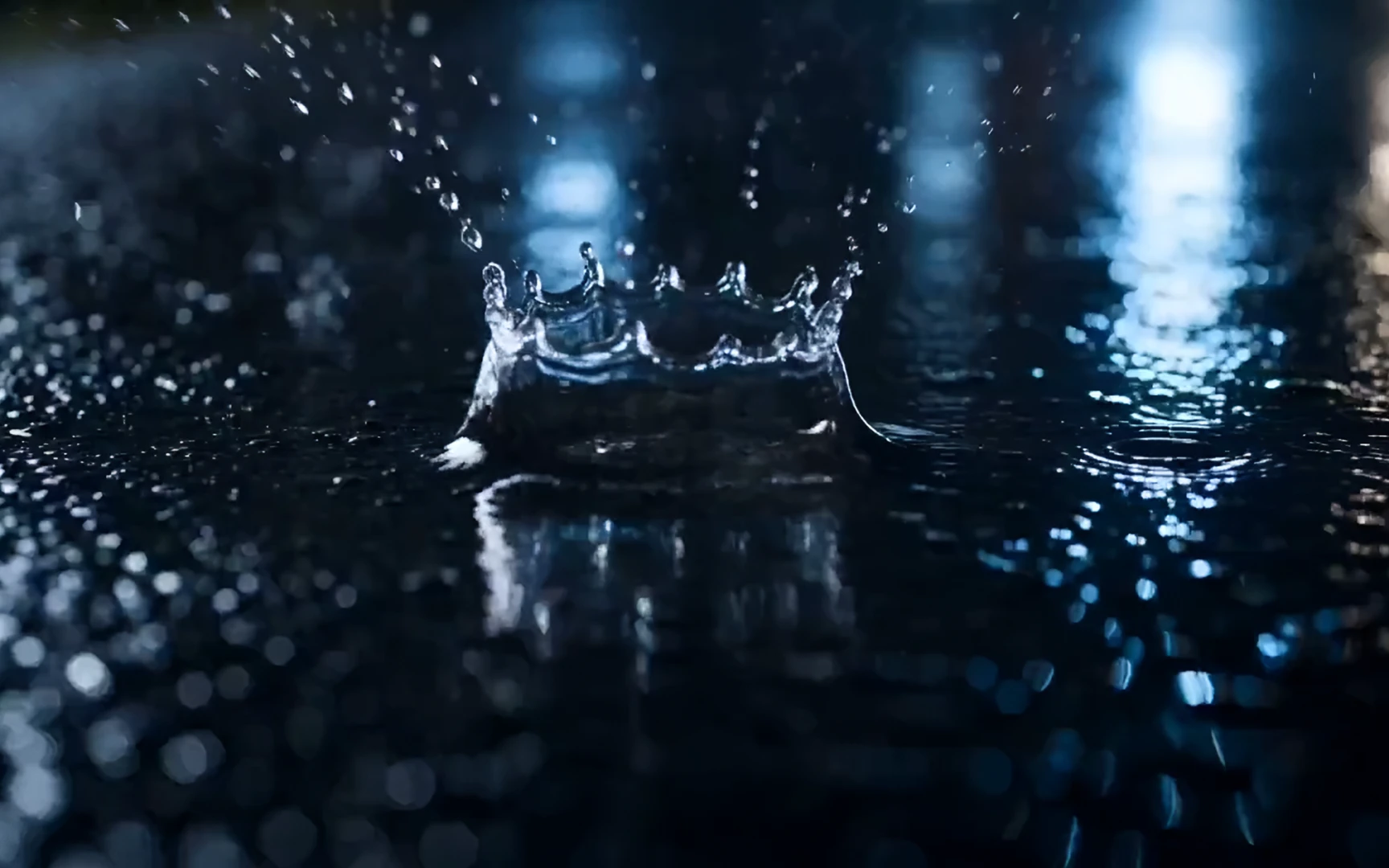 A raindrop splashing into a puddle on a night road, blue light behind