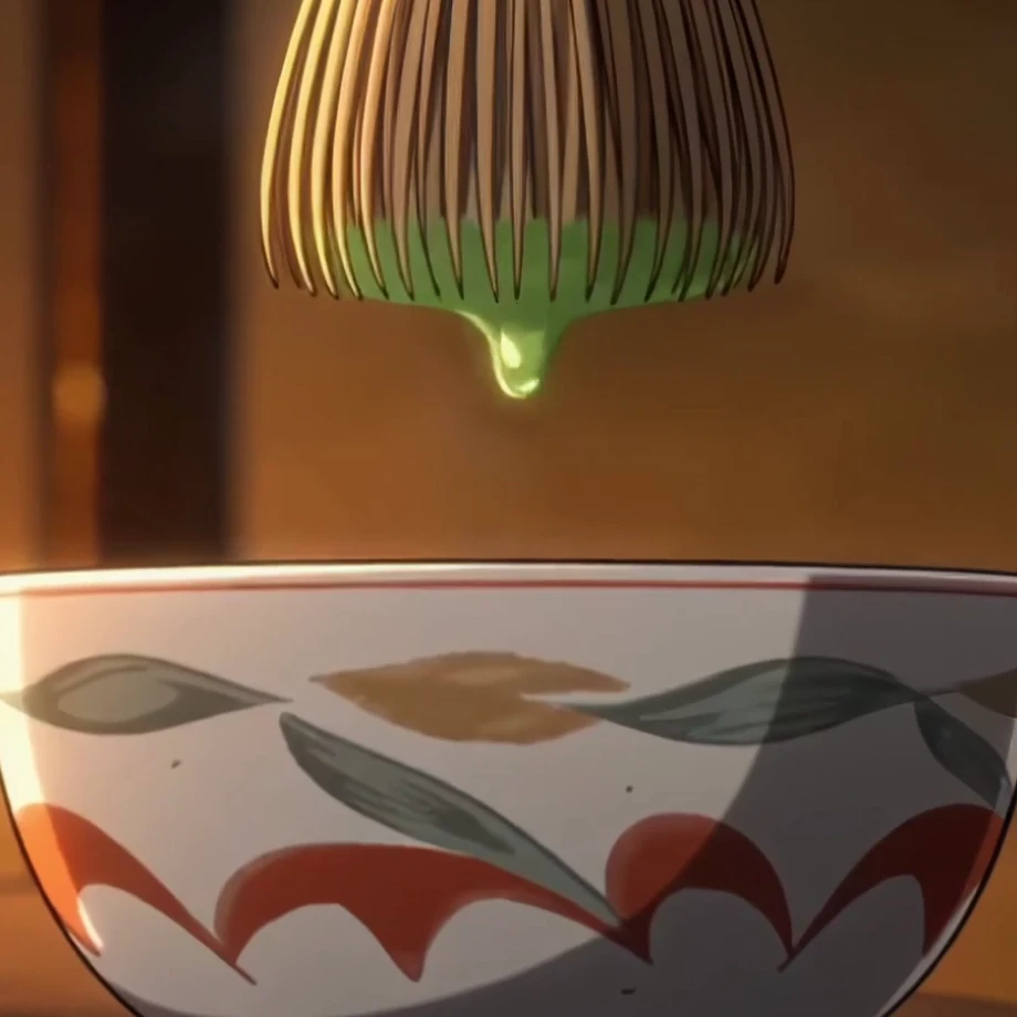 A painted white tea bowl with red and green leaves, a drop of matcha falling from the whisk above it