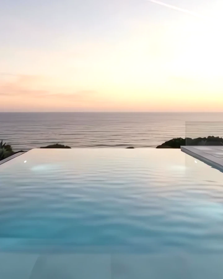 An infinity pool at the cliff edge, the sea and a pink sunset sky